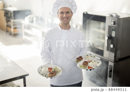 Smiling chef in uniform standing with ready meals in the kitchen 88449311