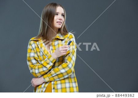 Studio shot of attractive smiling girl looking at camera and holding an electronic cigarette in a raised hand, isolated on grey-blue background 88449362