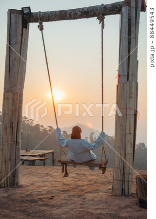 Loneliness woman sitting on the swing and looking at the sun at sunrise time. Loneliness woman sitting on the swing and looking at the sun at sunrise time. 88449543