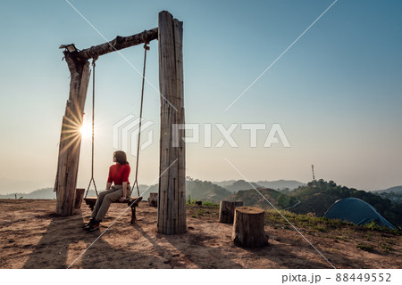 Loneliness woman sitting on the swing and looking at the sun at sunset time. 88449552