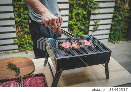 A man's hand grilling meat on the charcoal grill. 88449557