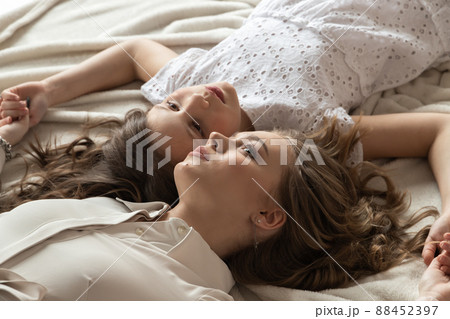 Real sisters lying on a bed, casual studio portrait of two beautiful European girls Real sisters lying on a bed, casual studio portrait of two beautiful European girls 88452397