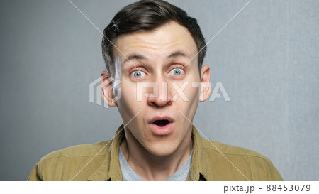 Handsome guy with stylish hairdo surprised to camera over grey background. 88453079