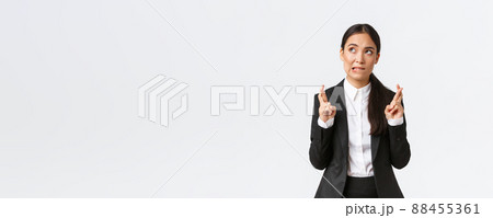 Hopeful asian businesswoman looking worried, biting lip and cross fingers good luck, making wish, anticipating big contract or deal, worried about outcome, standing white background 88455361