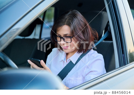 Confident female driver with smartphone driving a car Confident female driver with smartphone driving a car 88456014