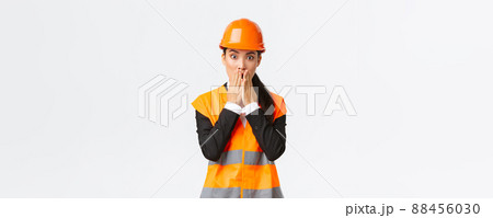 Concerned and worried asian female engineer having problem at construction area, gasping and cover mouth shocked, stare at camera startled with alarmed expression, wearing safety helmet Concerned and worried asian female engineer having problem at construction area, gasping and cover mouth shocked, stare at camera startled with alarmed expression, wearing safety helmet 88456030