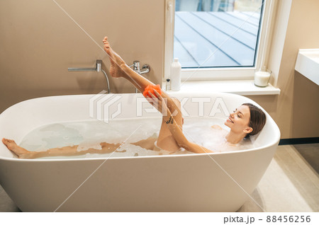 Cheerful woman washing herself with a soapy loofah 88456256