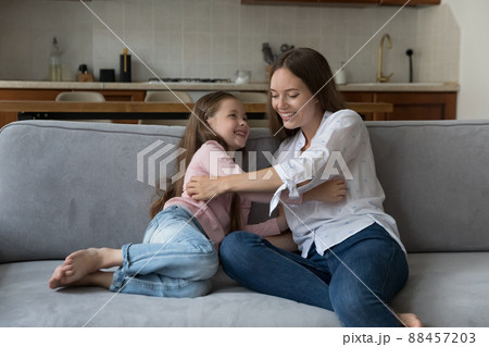 Happy playful mom tickling excited daughter girl on sofa 88457203