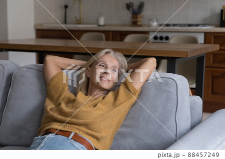 Happy peaceful blonde mature 50s woman resting on comfortable sofa 88457249