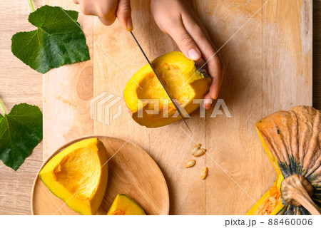 Hand holding kitchen knife and cutting Asian pumpkin on wooden board, Table top view Hand holding kitchen knife and cutting Asian pumpkin on wooden board, Table top view 88460006