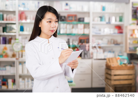Chinese female looking medicine with notebook near shelves in pharmacy Chinese female looking medicine with notebook near shelves in pharmacy 88462540