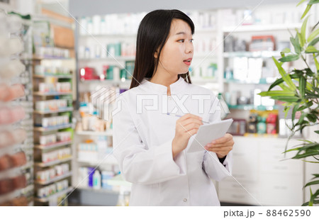 Chinese female looking medicine with notebook near shelves in pharmacy 88462590