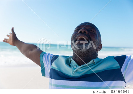 Happy african american senior retired man with eyes closed and arms outstretched at beach 88464645