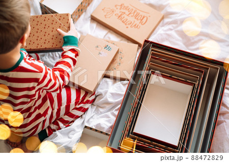 Child in striped pajamas standing next to open boxes on white bed Child in striped pajamas standing next to open boxes on white bed 88472829