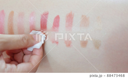 Hand wiping off lipstick patches drawn on a skin, with a piece cotton pad. 88473468