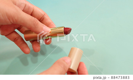 Hand holding a tube of red lipstick, with the other hand holding the lid. 88473883