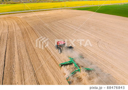 Aerial View. Tractor Plowing Field. Beginning Of Agricultural Spring Season. Cultivator Pulled By A Tractor In Countryside Rural Field Landscape. Dust Rises From Under Plows Aerial View. Tractor Plowing Field. Beginning Of Agricultural Spring Season. Cultivator Pulled By A Tractor In Countryside Rural Field Landscape. Dust Rises From Under Plows 88476843
