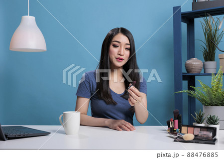 Smiling attractive content creator talking with fans presenting makeup lipstick while recording creative tutorial for beauty podcast channel. Social media influencer advertising cosmetic product 88476885