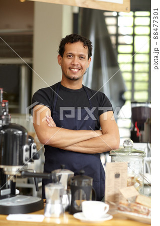 Hes a master fo brewing. Shot of a handsome barista standing behind his coffee bar with his arms crossed. 88477301