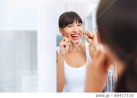 Flossing away. Shot of a cheerful attractive young woman flossing her teeth while looking at her reflexion in a mirror at home. 88477510