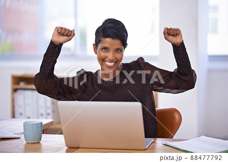 Her business is reaching new heights. A portrait of a beautiful young woman sitting in her office and raising her arms enthusiastically. 88477792