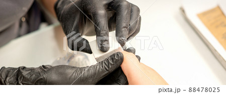 Close up of the caucasian hands of a professional manicurist are filing the nails of a young woman. Young caucasian woman receiving a manicure by a beautician with a nail file in a nail salon 88478025