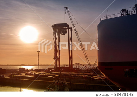 Port scene in the late afternoon with a large sun disk behind the stern of a freighter and a container crane Port scene in the late afternoon with a large sun disk behind the stern of a freighter and a container crane 88478148