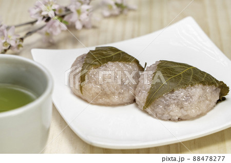 木目調バックで白い皿にのっている桜もちと桜と緑茶寄り 88478277