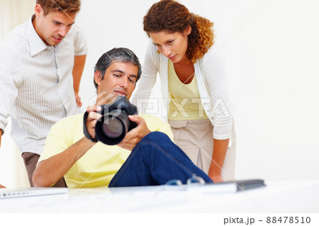 Photographers looking at pictures in camera. Male photographer showing pictures to his colleagues in his camera. 88478510