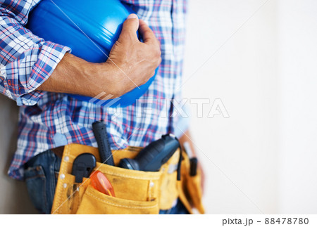 Construction worker holding protective helmet. Mid section of construction worker with tool belt holding blue protective helmet. 88478780