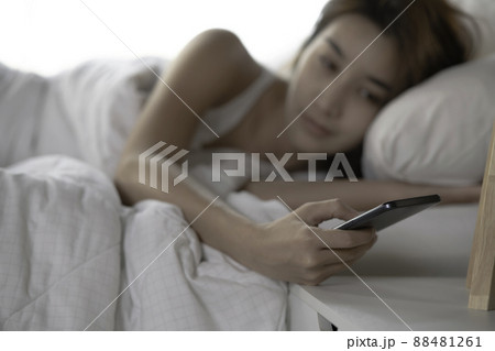 Asian woman using smartphone checking social media feeling happy smiling while lying on bed  88481261