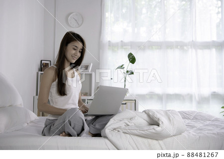 Beautiful Asian woman in pyjamas using laptop sitting on the bed in the house. Beautiful Asian woman in pyjamas using laptop sitting on the bed in the house. 88481267