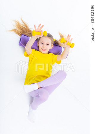 Little cute happy girl lies with dumbbells and gymnastic mat. Isolated on white background. View from above. 88482196
