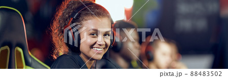 Professional gamer. Side view of a happy mixed race teenage girl wearing headphones looking at camera and smiling while participating in eSport tournament 88483502