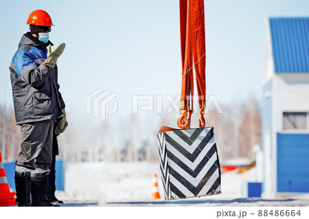 Slinger in helmet works outside. Signal to lift load up. Long workflow. Work of slinger in winter in 88486664