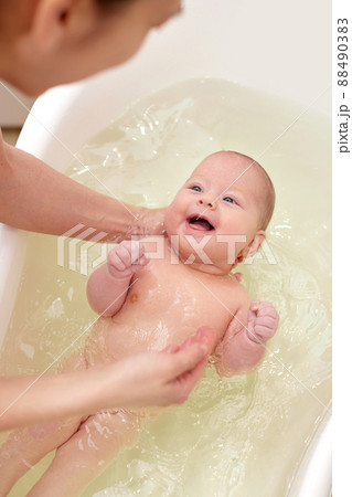 mother bathes her baby in a white small plastic tub mother bathes her baby in a white small plastic tub 88490383