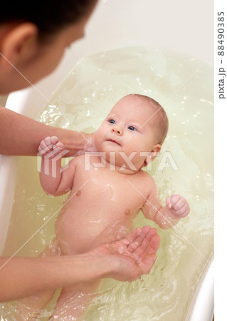 mother bathes her baby in a white small plastic tub 88490385