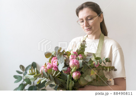Portrait of a professional florist of a young woman in glasses with a bouquet of bright flowers. The concept of small business and young entrepreneur Portrait of a professional florist of a young woman in glasses with a bouquet of bright flowers. The concept of small business and young entrepreneur 88490811