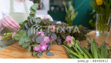 Woman in an apron works with flowers in a beautiful store. Sale of bouquets in Internet. Online order for delivery of a gift 88490812