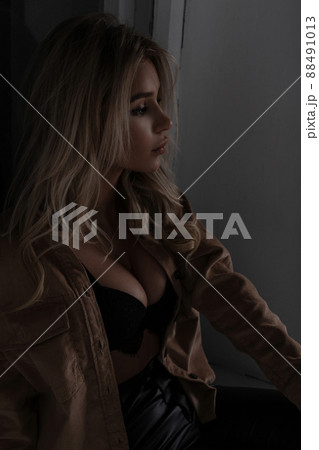 Glamor sexy stylish woman with beautiful lush breasts in a luxurious lace bra in fashionable leather pants in a vintage vilyurovoy shirt posing in a room near the window. Charming sensual girl blonde. 88491013