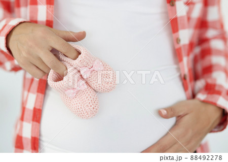 Pregnant woman holds pink baby slippers on stomach closeup Pregnant woman holds pink baby slippers on stomach closeup 88492278