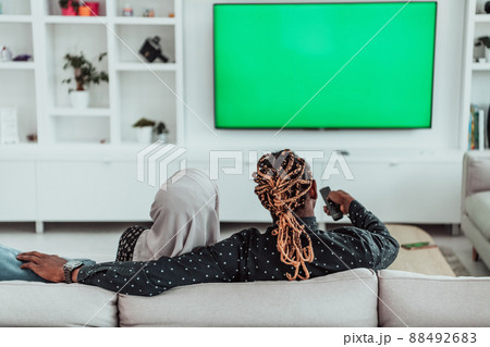 African Couple Sitting On Sofa Watching TV Together Chroma Green Screen Woman Wearing Islamic Hijab Clothes 88492683