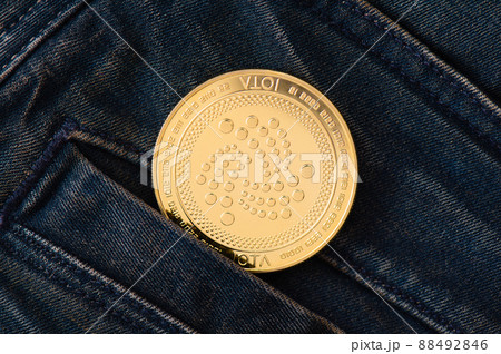 A physical golden IOTA coin sticks out of the pocket of blue frayed jeans. 88492846