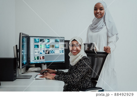 Friends at the office two young Afro American modern Muslim businesswomen wearing scarf in creative bright office workplace with a big screen Friends at the office two young Afro American modern Muslim businesswomen wearing scarf in creative bright office workplace with a big screen 88492929