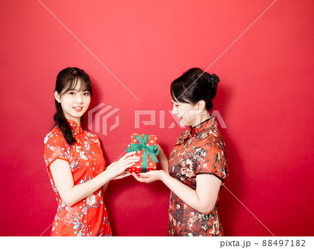 Daughter wearing traditional cheongsam qipao is congratulating mom and giving present wrapped in gift box. Family holiday and togetherness. 88497182