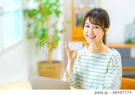 リビングでネットショッピングするカードを持ったカメラ目線の若い主婦 88497774