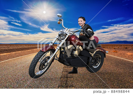 ツーリング中、道の真ん中でバイクに座り、笑顔でこちらを見ている女性ライダー。 88498844