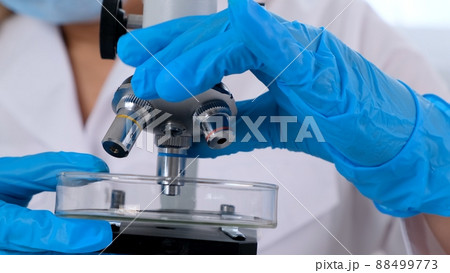 Hands of a researcher laboratory assistant in protective gloves holding a microscope in the 88499773