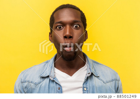 Portrait of excited funny man in denim shirt making fish face with lips and big amazed eyes, looking surprised and silly at camera, wondered expression. studio shot isolated on yellow background 88501249