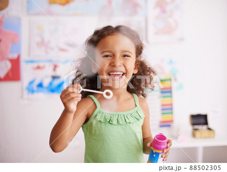 Bubbles that pop are funny. Shot of an adorable little girl blowing bubbles in her bedroom. 88502305